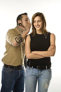Caucasian mid-adult man whispering into ear of teen female.