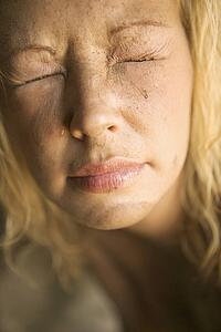 Close-up of blond womans muddy face with closed squinting eyes.