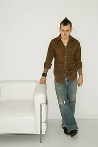 Man with mohawk standing beside white chair 