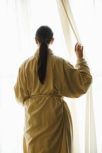 Taiwanese mid adult woman in bathrobe looking out window.