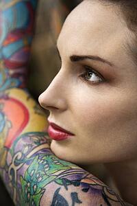 Close-up of attractive Caucasian woman's face and tattooed arm.