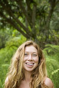 Beautiful happy Caucasian young adult woman in lush forest smiling and looking at viewer.