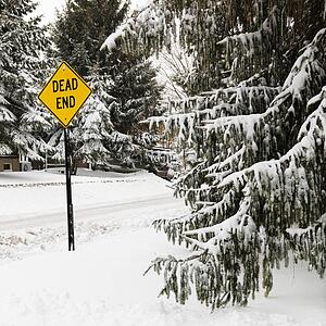 Snowy street scene in suburb with evergreen trees and dead end road sign.