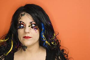 Portrait of Caucasian woman with unique makeup and hair against orange background.