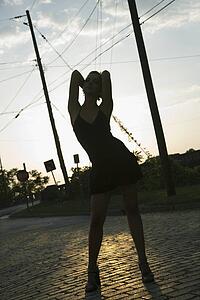 Silhouette adult blonde woman wearing little black dress posing in street.
