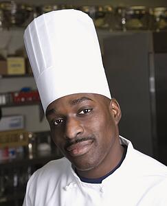 Head shot of chef wearing traditional uniform and toque looking at viewer.