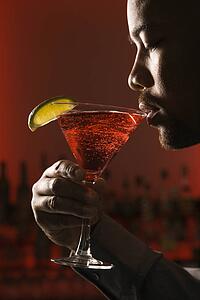 Man drinking martini in bar against glowing red background.