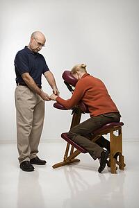 Middle-aged male massage therapist massaging hands of middle-aged woman sitting in massage chair