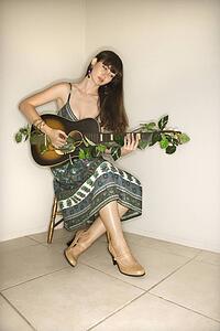 Young adult Caucasian woman sitting playing guitar.