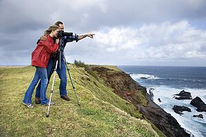 Couple looking off the coast through a camera on a tripod 