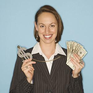 Caucasian businesswoman smiling holding money and wearing necklace with oversized dollar sign.