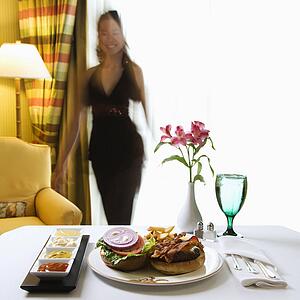 Room service cheeseburger meal with flowers and woman in background