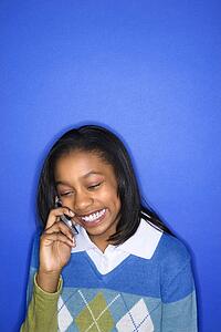 Portrait of African-American teen girl talking on cellphone smiling standing in front of blue background.