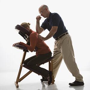 Massage therapist massaging back of woman sitting in massage chair