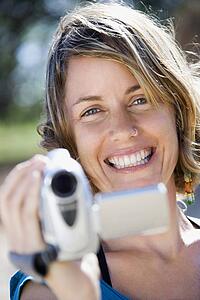 Mid-adult Caucasian woman outdoors pointing video camera at viewer.