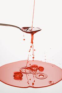 Stream of red cough syrup overflowing spoon into puddle below.