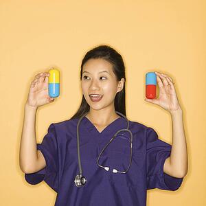 Asian Chinese mid-adult female doctor holding up giant pills against yellow background smiling.