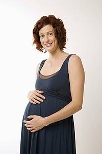 Portrait of Caucasion mid-adult pregnant woman with hands on belly looking at viewer and smiling.