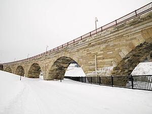 Scene of stone bridge over over snow covered road.