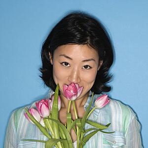 Head and shoulder portrait of pretty woman smelling flowers on blue background