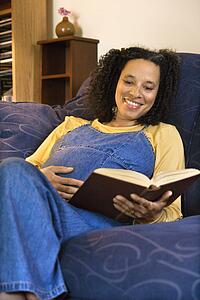 Portrait of pregnant female reading a book and holding her stomach.