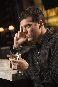 Side view of mid adult man holding martini with hand to head thinking