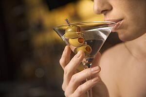 Close up of mid adult Caucasian woman drinking a martini with three olives.