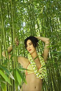 Young adult woman standing in bamboo forest wearing bikini and lei.