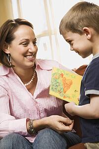Caucasian boy giving mid adult mother a drawing.