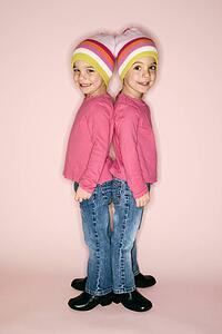 Young female twin girls standing back to back.