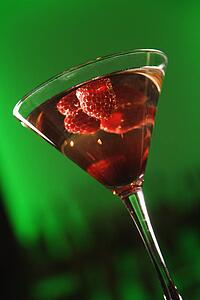 Still life of martini cocktail with raspberries fruit against glowing green background