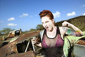 Angry tattooed Caucasian woman yelling with fists clenched in junkyard.