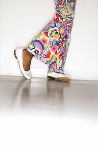 Girl's legs with floral pants and white shoes against white background.
