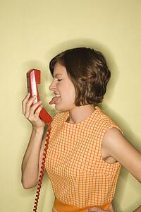 Pretty Caucasian mid-adult woman wearing orange dress sticking out tongue at red telephone receiver.