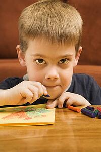 Caucasian boy drawing with crayons and looking at viewer.