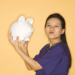 Female doctor holding piggy bank against yellow background scrunching nose and looking at viewer.
