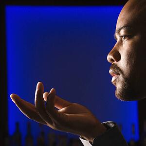 Man against glowing blue background holding out hand in gesture.