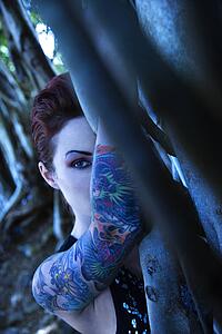Blue-toned portrait of tattooed Caucasian woman hiding behind Banyan tree 