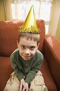Caucasian boy with party hat looking at viewer and making facial expression.
