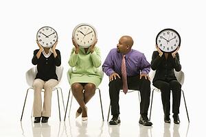 Businesswomen sitting holding clocks over faces while businessman looks on