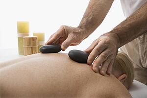 Massage therapist placing hot stones on back of woman
