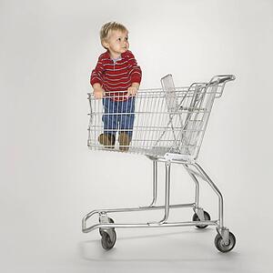 Studio portrait of young boy standing alone in empty shopping cart against white background.