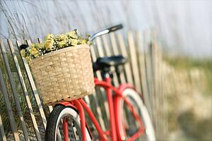 Red vintage bicycle with basket and flowers leaning against wooden fence at beach.