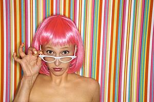 Woman wearing pink wig peeking over glasses 