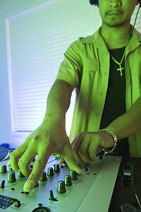 Close-up of young adult male DJ with hand on control panels of mixing equipment
