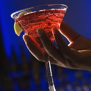 Male hand holding martini in bar against glowing blue background