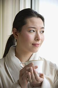 Mid adult woman in bathrobe drinking coffee and looking out window
