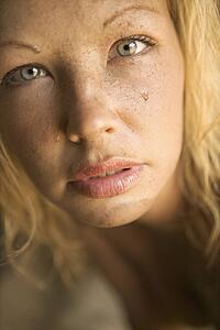 Close-up of blond womans muddy face looking at viewer.