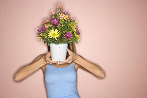 Female holding pot of flowers in front of her face
