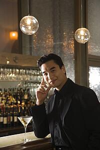 Young man standing at bar with cocktail.